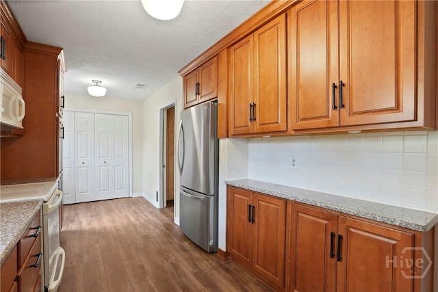 13609 Rockingham Ct, Savannah, GA 31419 - kitchen featuring white appliances, brown cabinets, decorative backsplash, dark wood-type flooring, and a textured ceiling
