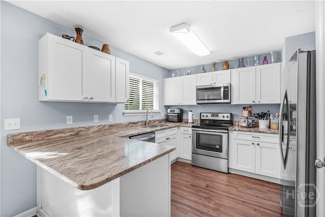 139 Crossover Ln, Savannah, GA 31410 - kitchen featuring appliances with stainless steel finishes, a peninsula, light stone counters, white cabinets, and light wood finished floors