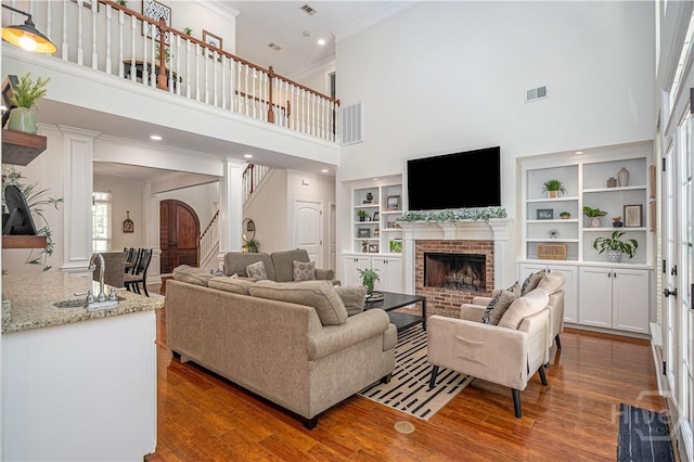 210 Windsong Dr, Richmond Hill, GA 31324 - living room featuring ornamental molding, a towering ceiling, a brick fireplace, wood finished floors, and stairway