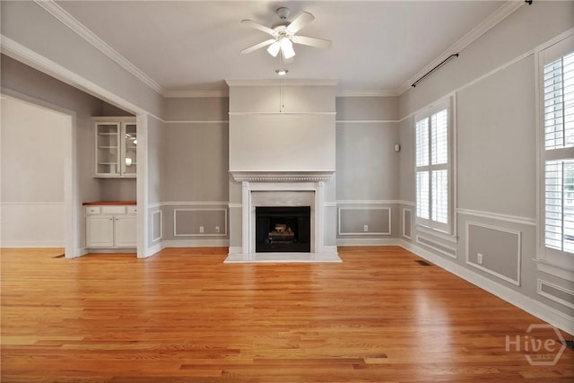 536 E Harris St, Savannah, GA 31401 - unfurnished living room featuring ceiling fan, light wood finished floors, a fireplace with raised hearth, a decorative wall, and crown molding