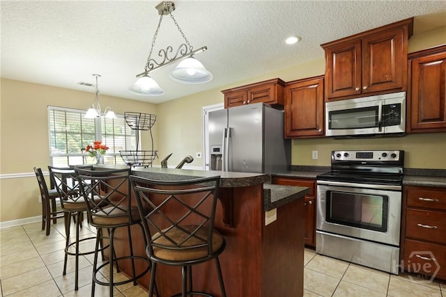 140 Kettle Creek Ln, Midway, GA 31320 - kitchen featuring appliances with stainless steel finishes, dark countertops, light tile patterned floors, a textured ceiling, and a kitchen island