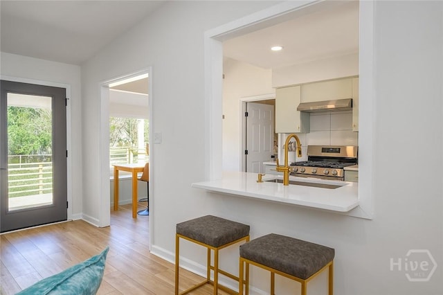 27 Bryan Wood Cir, Savannah, GA 31410 - kitchen with gas stove, range hood, light wood-style flooring, a kitchen breakfast bar, and light countertops