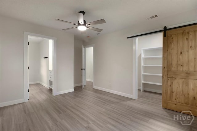 114 Paradise Dr, Savannah, GA 31406 - unfurnished bedroom featuring a spacious closet, a barn door, light wood-style flooring, and a ceiling fan