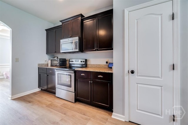 172 Green Paddock Cir, Guyton, GA 31312 - kitchen with appliances with stainless steel finishes, arched walkways, light wood finished floors, dark brown cabinets, and light stone countertops