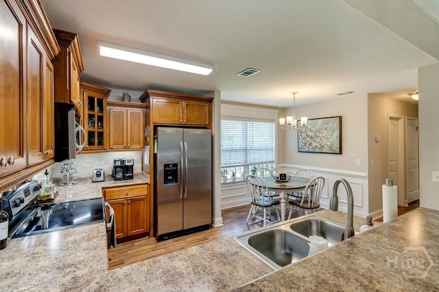 160 Wild Honey Ct, Richmond Hill, GA 31324 - kitchen with stainless steel appliances, brown cabinets, a chandelier, glass insert cabinets, and decorative light fixtures