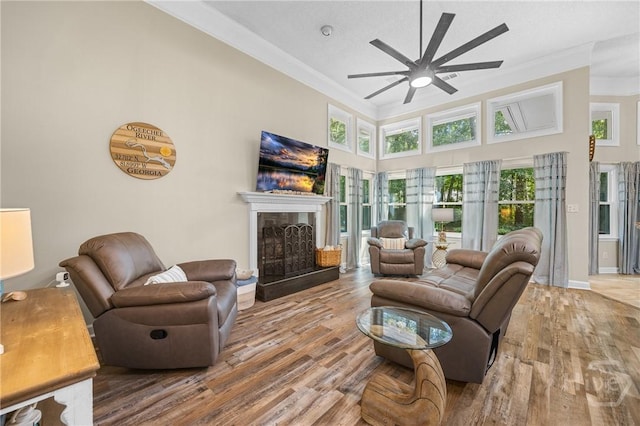 139 Mingarry Dr, Richmond Hill, GA 31324 - living room featuring a ceiling fan, a towering ceiling, wood finished floors, a fireplace with raised hearth, and ornamental molding