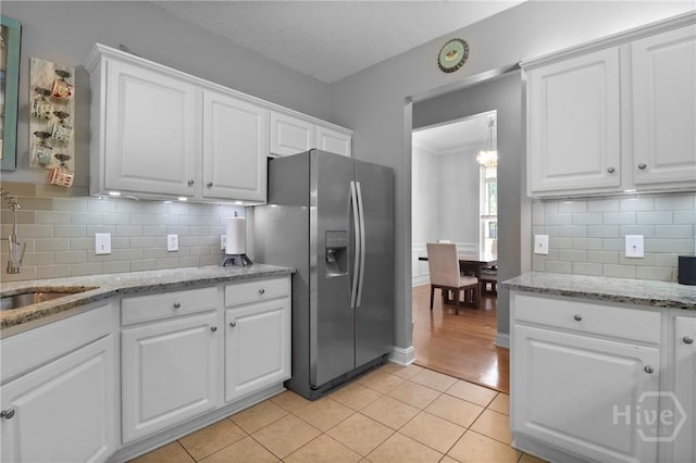 204 Bristol Way, Richmond Hill, GA 31324 - kitchen with stainless steel fridge, white cabinets, a chandelier, and light tile patterned flooring