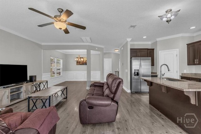 1237 Cypress Fall Cir, Hinesville, GA 31313 - living room with a chandelier, light wood-type flooring, a ceiling fan, a wainscoted wall, and ornamental molding