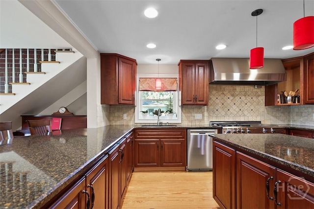 606 Rivers End Dr, Savannah, GA 31406 - kitchen featuring wall chimney exhaust hood, stainless steel appliances, decorative light fixtures, dark stone countertops, and light wood-style flooring