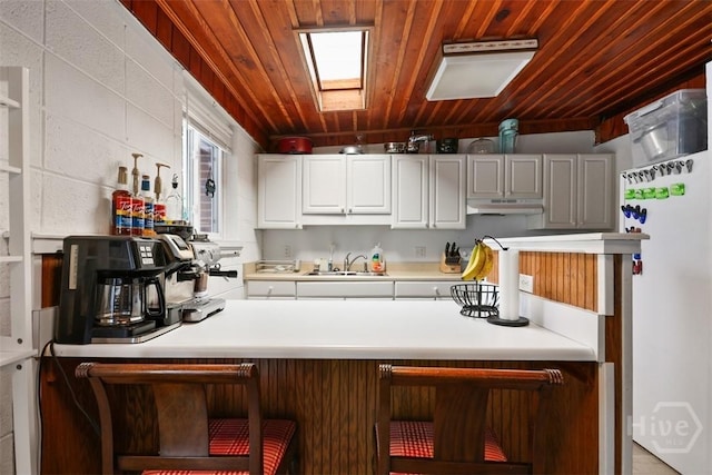 606 Rivers End Dr, Savannah, GA 31406 - kitchen featuring under cabinet range hood, wood ceiling, light countertops, a breakfast bar area, and white cabinetry