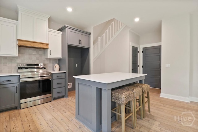 178 Cubbedge Dr, Rincon, GA 31326 - kitchen with stainless steel range with electric stovetop, gray cabinets, custom range hood, light wood finished floors, and backsplash