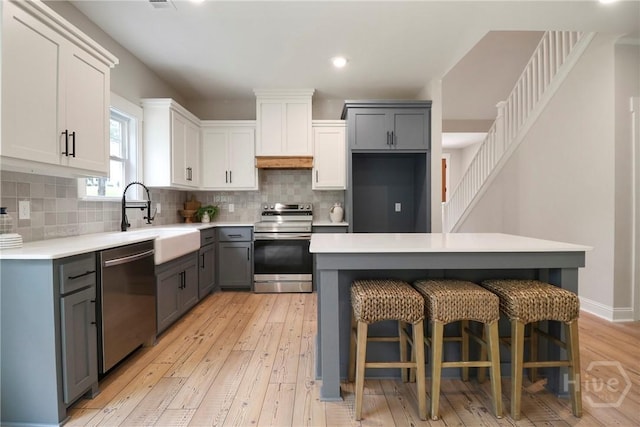 178 Cubbedge Dr, Rincon, GA 31326 - kitchen featuring appliances with stainless steel finishes, gray cabinetry, light wood-type flooring, tasteful backsplash, and a kitchen breakfast bar