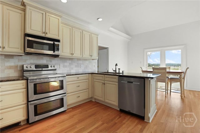 271 Davis Rd, Richmond Hill, GA 31324 - kitchen featuring cream cabinets, appliances with stainless steel finishes, a peninsula, backsplash, and vaulted ceiling