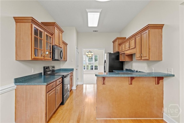 41 Patriot Dr, Richmond Hill, GA 31324 - kitchen with black appliances, a breakfast bar area, light wood finished floors, glass insert cabinets, and a peninsula