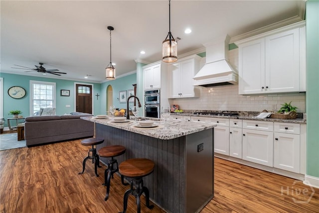 523 Goodman Dr, Midway, GA 31320 - kitchen with premium range hood, a kitchen breakfast bar, wood finished floors, white cabinets, and recessed lighting