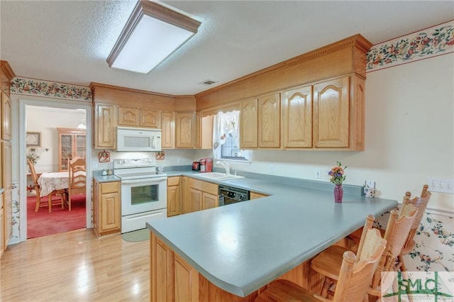 kitchen featuring kitchen peninsula, white appliances, light colored carpet, sink, and a breakfast bar area