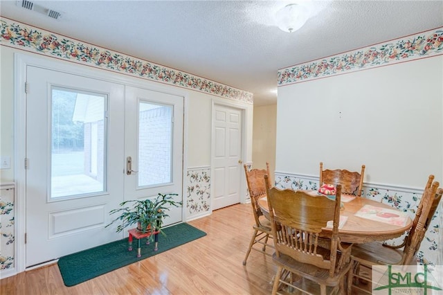 dining room with a textured ceiling, french doors, and light wood-type flooring