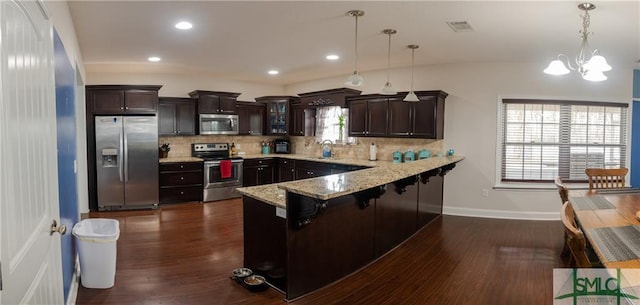 kitchen featuring appliances with stainless steel finishes, hanging light fixtures, dark brown cabinets, and tasteful backsplash