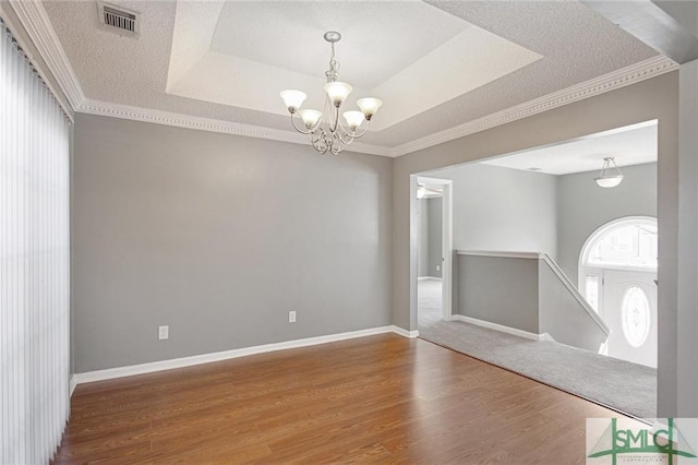 spare room with an inviting chandelier, dark wood-type flooring, ornamental molding, and a tray ceiling