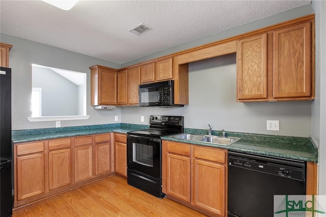 kitchen with sink, light wood-type flooring, black appliances, and a textured ceiling