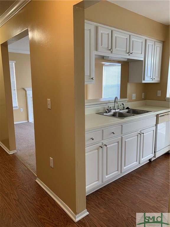 kitchen with dark carpet, white cabinets, crown molding, sink, and white dishwasher