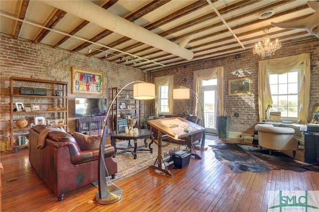 living room featuring plenty of natural light, brick wall, hardwood / wood-style floors, and a chandelier