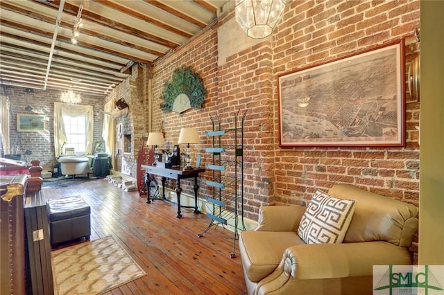 living room with brick wall, lofted ceiling with beams, a notable chandelier, and hardwood / wood-style flooring