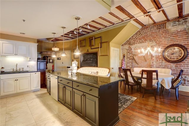 kitchen featuring brick wall, sink, white cabinets, dark stone countertops, and an inviting chandelier