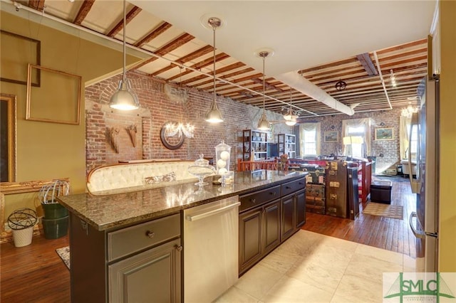 kitchen with a center island, brick wall, dark stone counters, dark brown cabinets, and appliances with stainless steel finishes