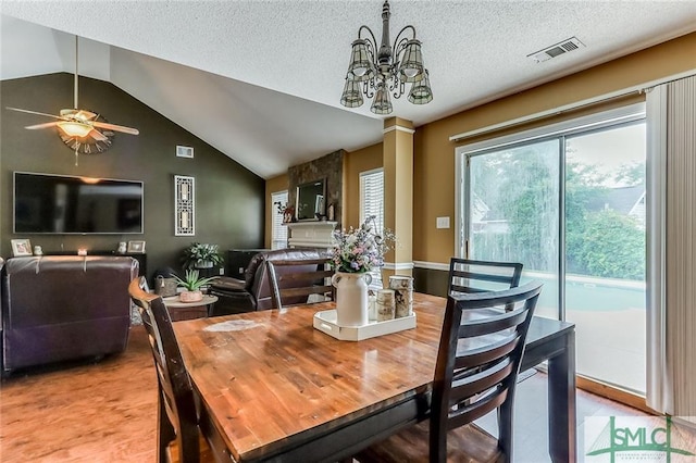 dining area featuring a fireplace, a textured ceiling, ceiling fan with notable chandelier, light hardwood / wood-style flooring, and lofted ceiling