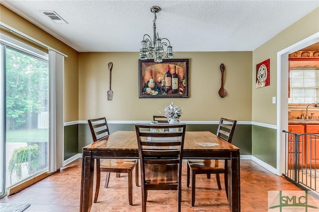 dining area with a healthy amount of sunlight, a textured ceiling, a notable chandelier, and light wood-type flooring