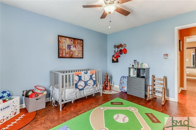 bedroom featuring ceiling fan, a crib, and dark wood-type flooring