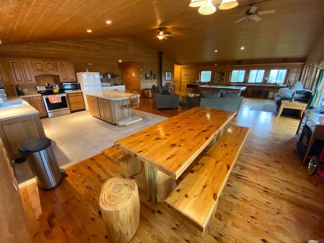 dining space featuring lofted ceiling, ceiling fan, light wood-type flooring, and wooden walls