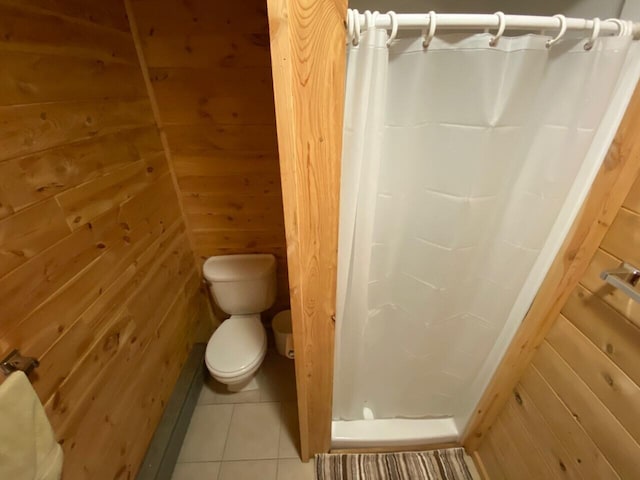 bathroom with toilet, wood walls, and tile flooring