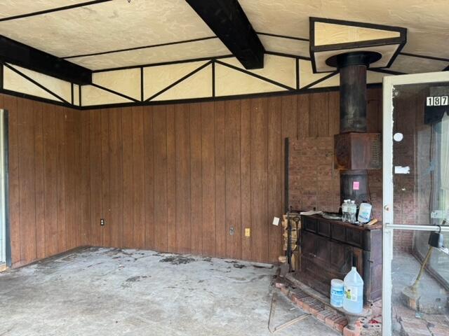 unfurnished living room featuring vaulted ceiling with beams, wooden walls, and a wood stove