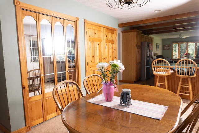 carpeted dining room featuring beam ceiling and ceiling fan with notable chandelier