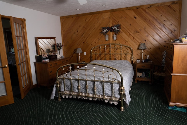 bedroom featuring a textured ceiling, wooden walls, ceiling fan, and dark carpet