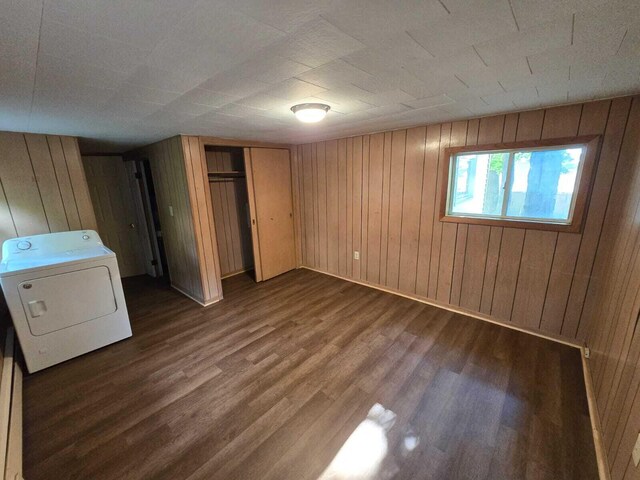 unfurnished bedroom featuring wood walls, a closet, washer / dryer, and dark hardwood / wood-style floors