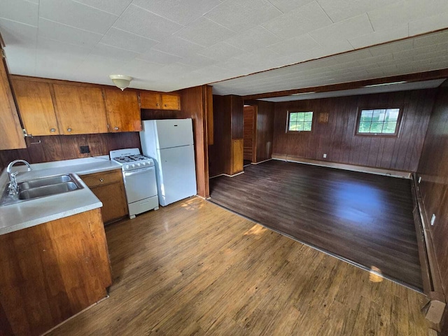 kitchen with dark wood-type flooring, wood walls, white appliances, and sink