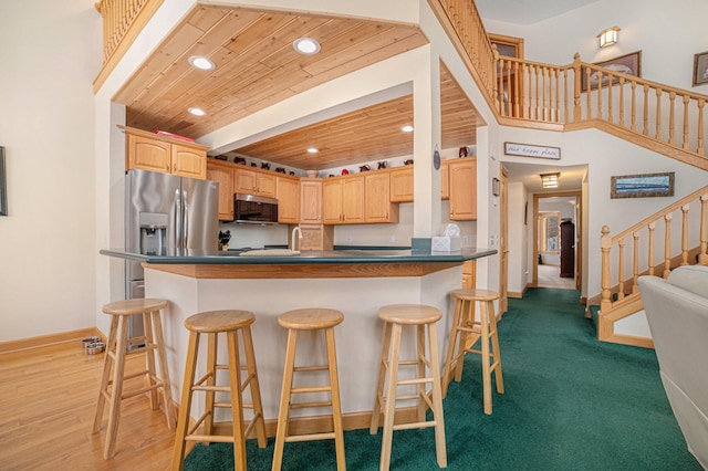 kitchen featuring carpet, a kitchen bar, light brown cabinets, and wood ceiling