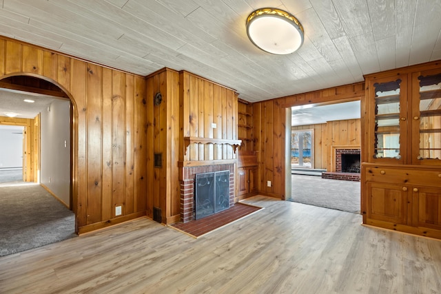 unfurnished living room with wooden walls, a fireplace, wood ceiling, and light hardwood / wood-style flooring