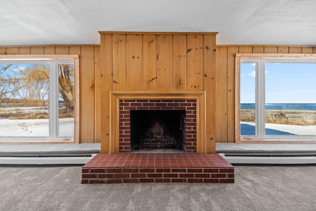 unfurnished living room with a brick fireplace, a textured ceiling, baseboard heating, wooden walls, and carpet floors