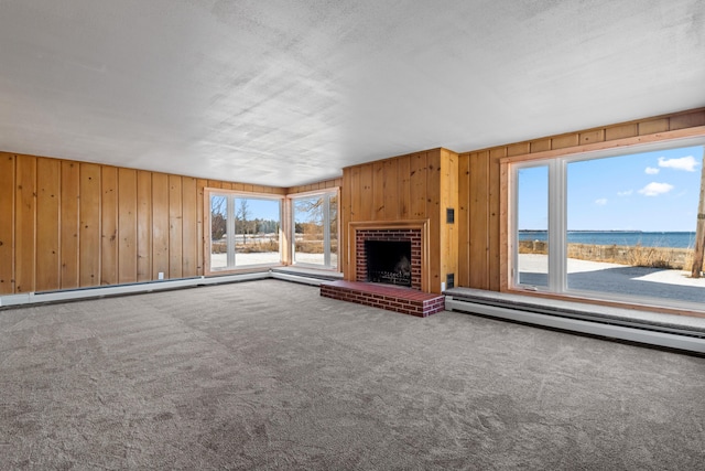 unfurnished living room featuring wood walls, a water view, a brick fireplace, carpet flooring, and a baseboard radiator