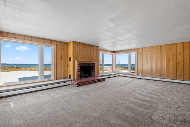 unfurnished living room featuring carpet flooring, wooden walls, a fireplace, and a water view