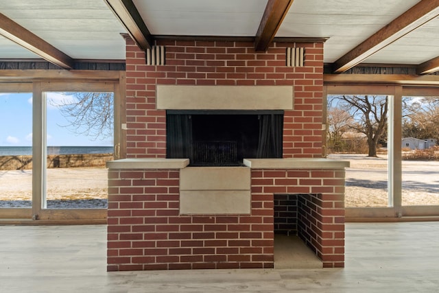 interior details featuring beam ceiling, a brick fireplace, and wood-type flooring