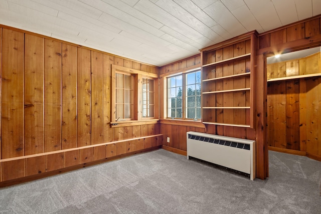 spare room featuring dark colored carpet, radiator heating unit, and wood walls