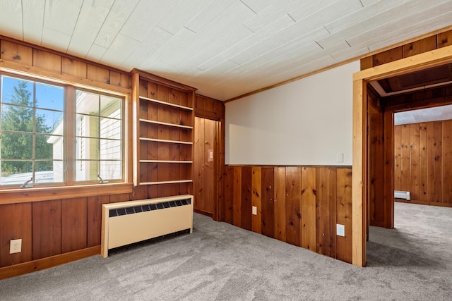 unfurnished room featuring carpet flooring, radiator, and wooden walls