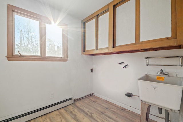 clothes washing area featuring light hardwood / wood-style floors, cabinets, sink, and a baseboard radiator