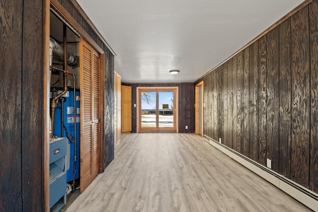 corridor with gas water heater, light hardwood / wood-style flooring, baseboard heating, and wood walls