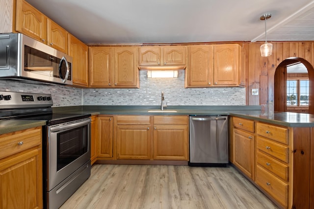 kitchen with sink, backsplash, pendant lighting, appliances with stainless steel finishes, and light wood-type flooring